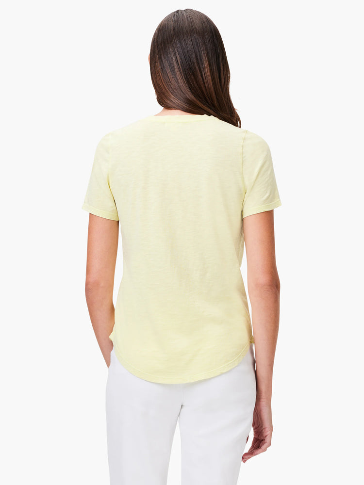 Pale yellow short-sleeve tee on a woman's back. Features textured fabric and rounded hem.
