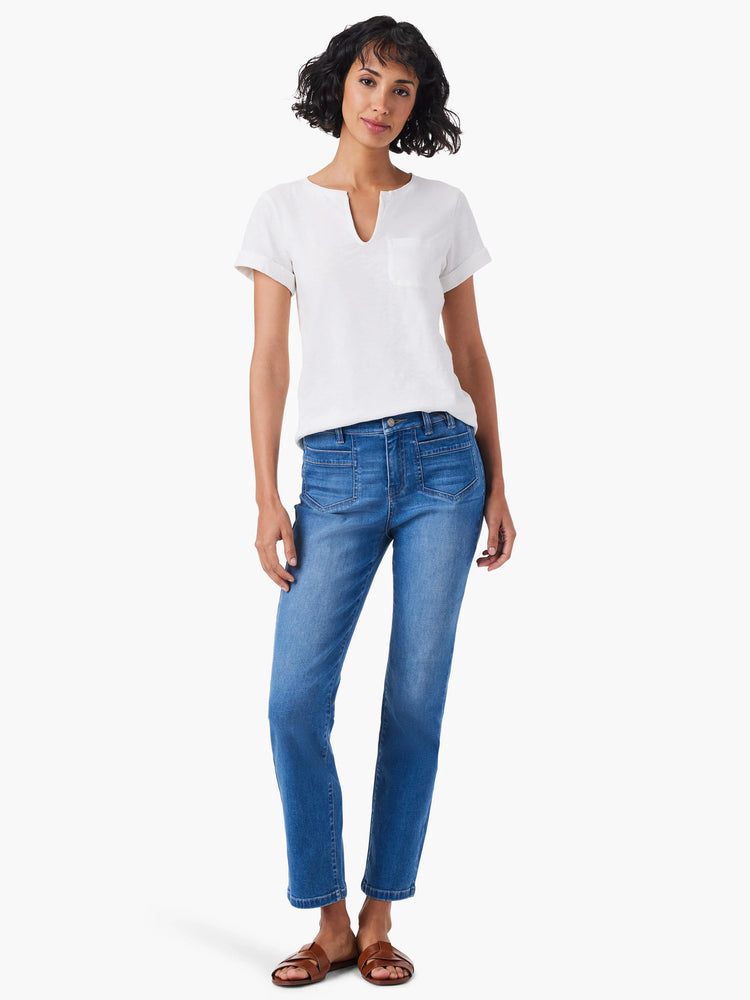 Woman wearing white split-neck tee, medium-wash blue jeans, and brown sandals.
