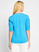 Back view of bright blue, elbow-sleeve shirt.  Ruched detailing on sleeves. Split neckline.
