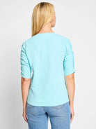 Light teal shirt, elbow-length sleeves with ruched detailing, split neckline.  Back view.