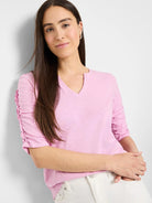 Light pink, elbow-length sleeves with ruched detailing at the shoulders, split v-neck.