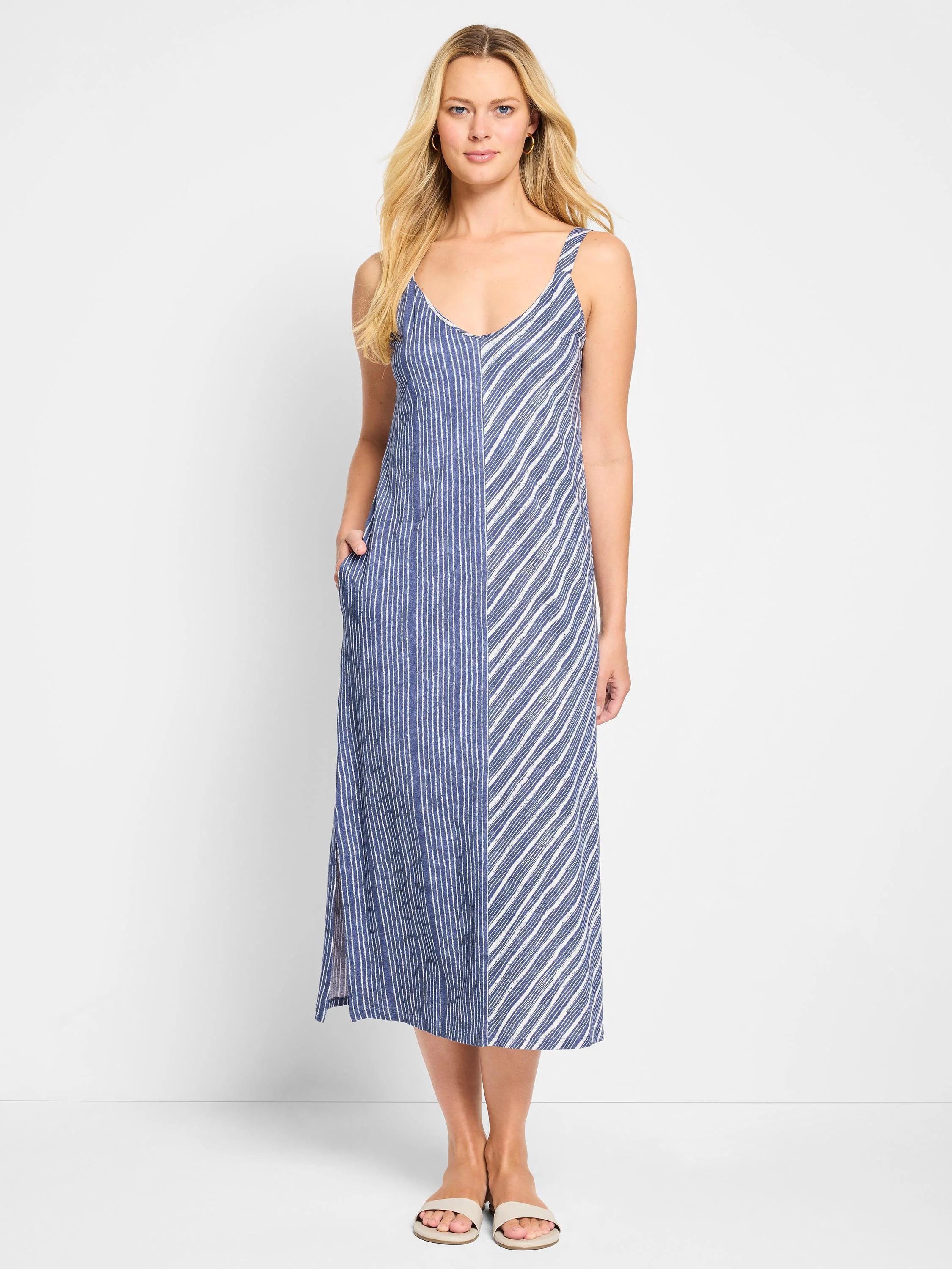 Mid-length sleeveless V-neck dress; blue and white mixed stripes, vertical on one side, diagonal on the other; side pockets.