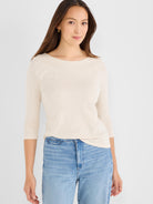 Model wears a fitted cream heathered knit top featuring three-quarter raglan sleeves and a wide boat neck.