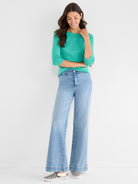 The look features a relaxed teal knit top with 3/4 sleeves and light blue high-rise wide-leg jeans.