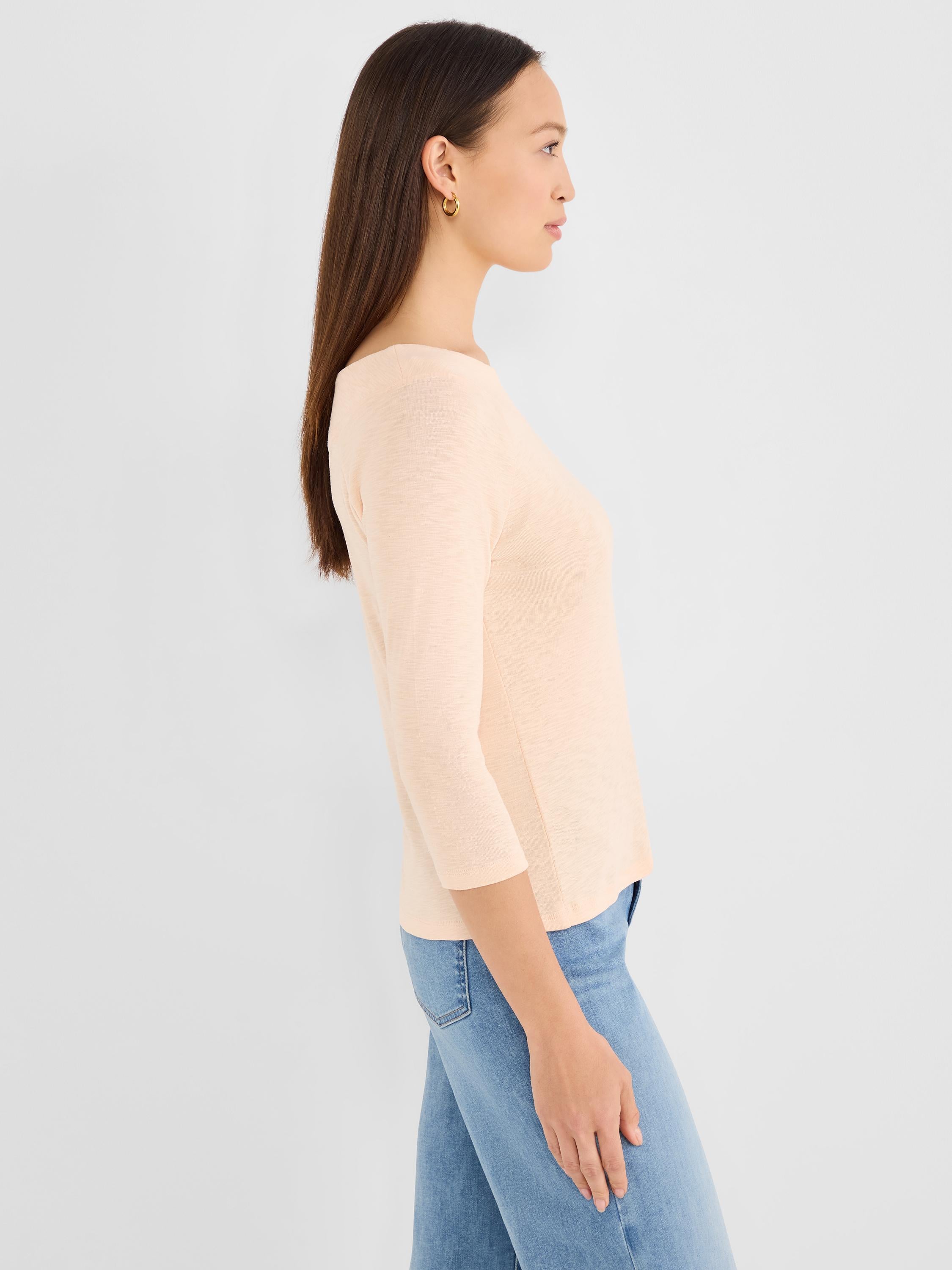 Model wears a fitted pale peach knit top featuring a boat neck and three-quarter length sleeves.