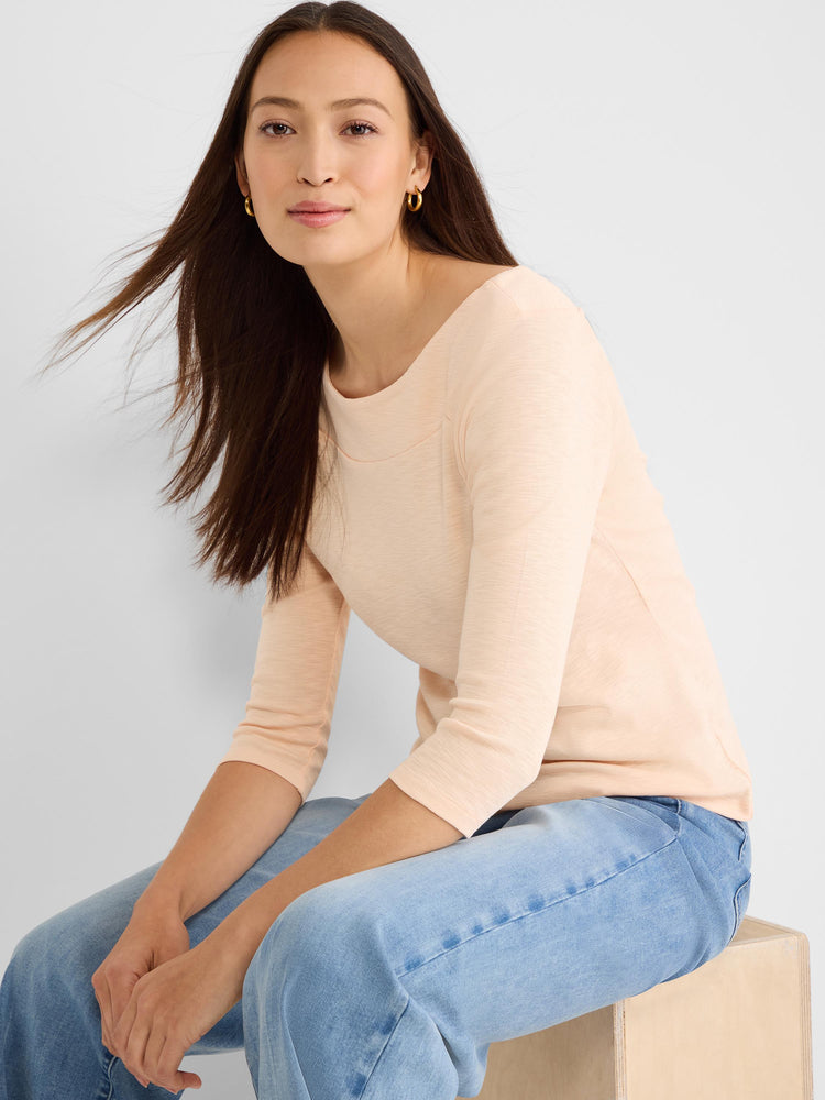 Model wears a soft peach knit shirt with three-quarter sleeves and a wide, flattering boat neck.