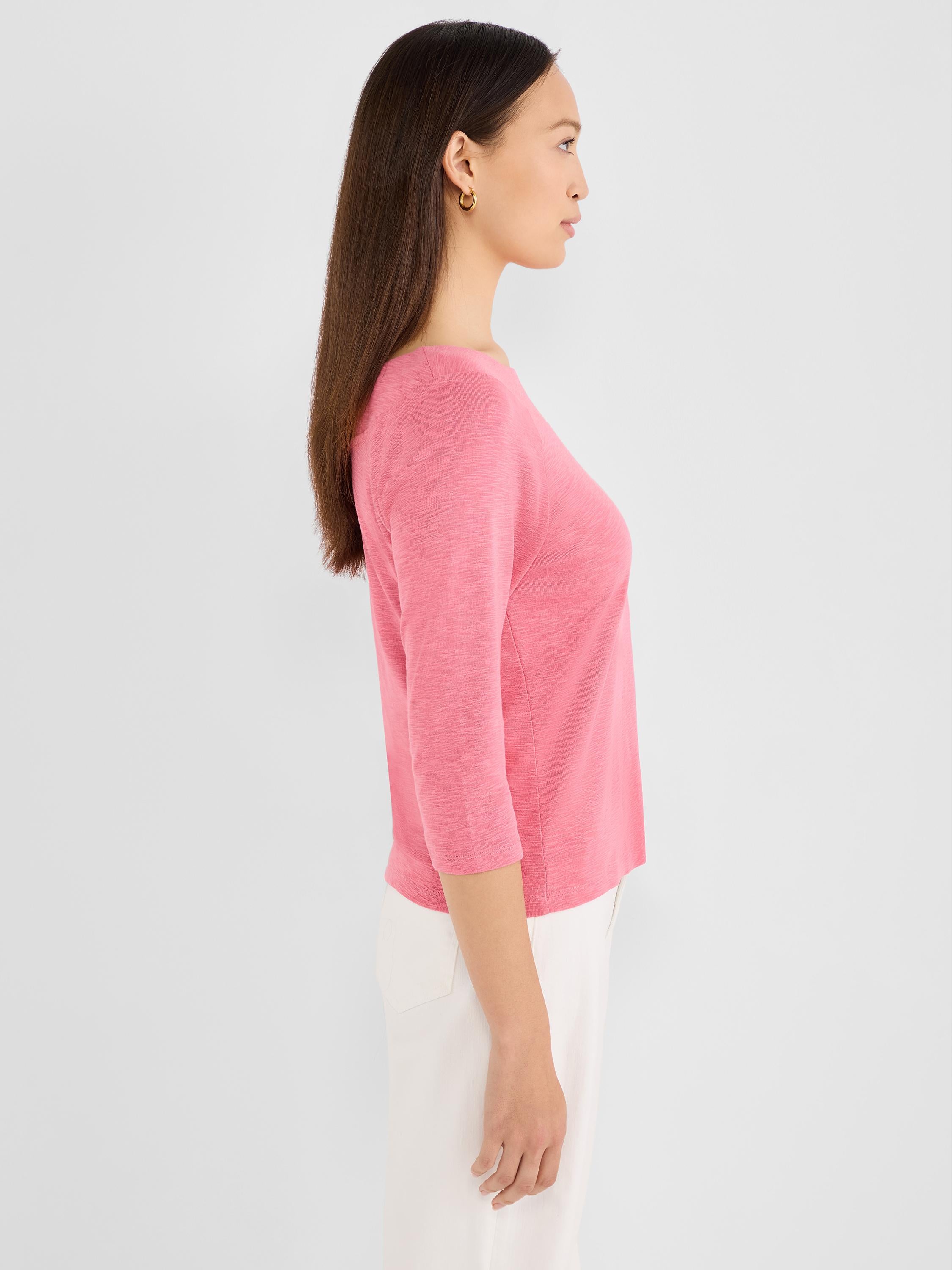 A model wears a fitted, heathered pink top featuring a boat neckline and three-quarter sleeves.