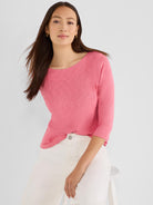 A model wears a relaxed pink textured knit top featuring three-quarter sleeves and a wide scoop neck.