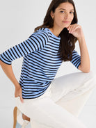 Relaxed fit blue and black Breton stripe knit top with three-quarter sleeves and a crew neck, styled with white pants.