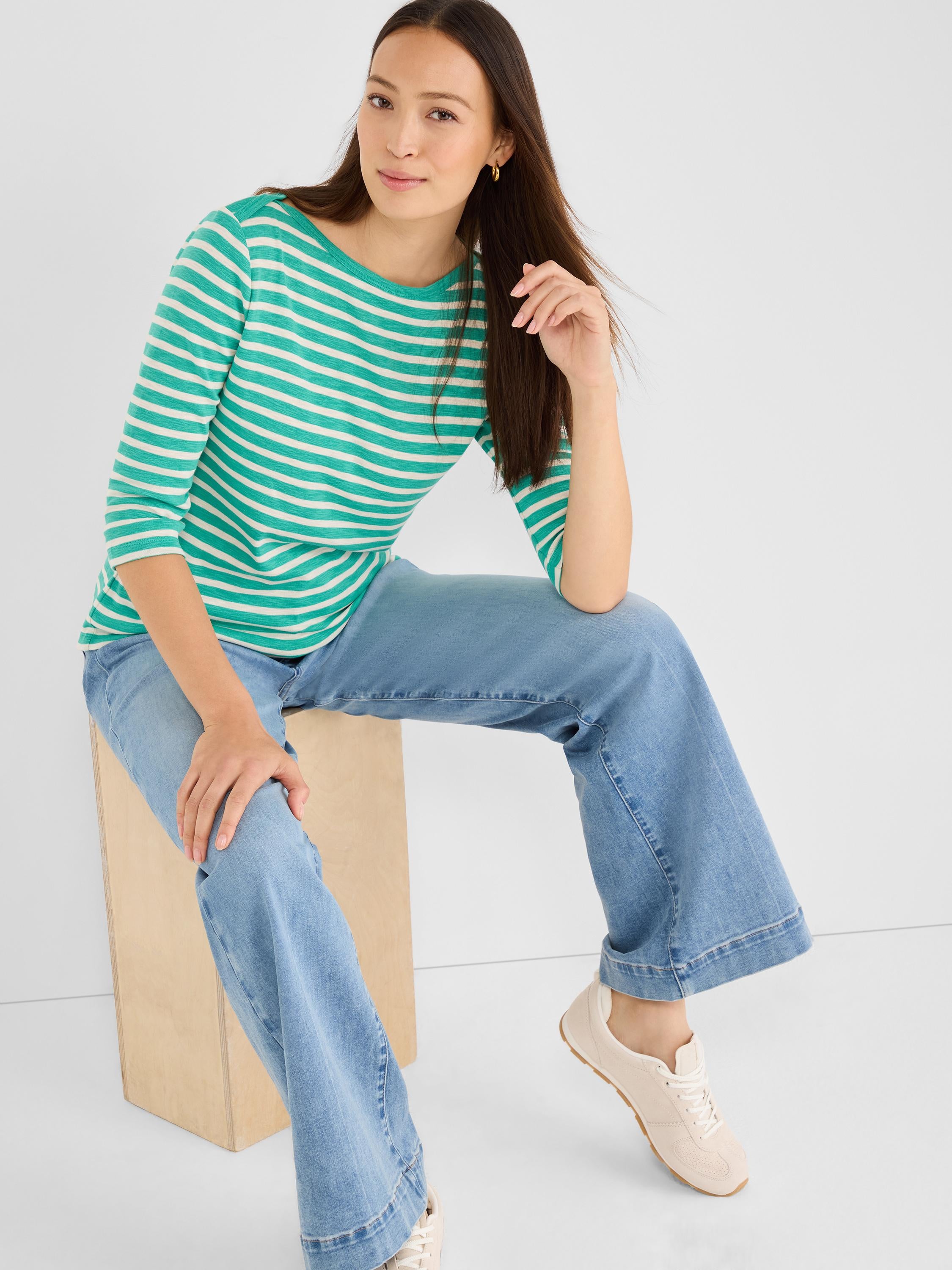 The model wears a striped green boatneck top and light wash wide-leg denim jeans.