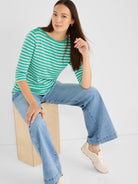 The model wears a striped green boatneck top and light wash wide-leg denim jeans.