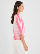 The model wears a relaxed fit tee in pink and white horizontal stripes, styled with 3/4 length sleeves.
