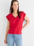 Red V-neck tee with cap sleeves, worn by a woman with dark hair and light blue jeans.