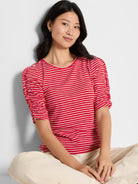 A fitted red and white striped knit top with a round neck and gathered, elbow-length ruched sleeves.