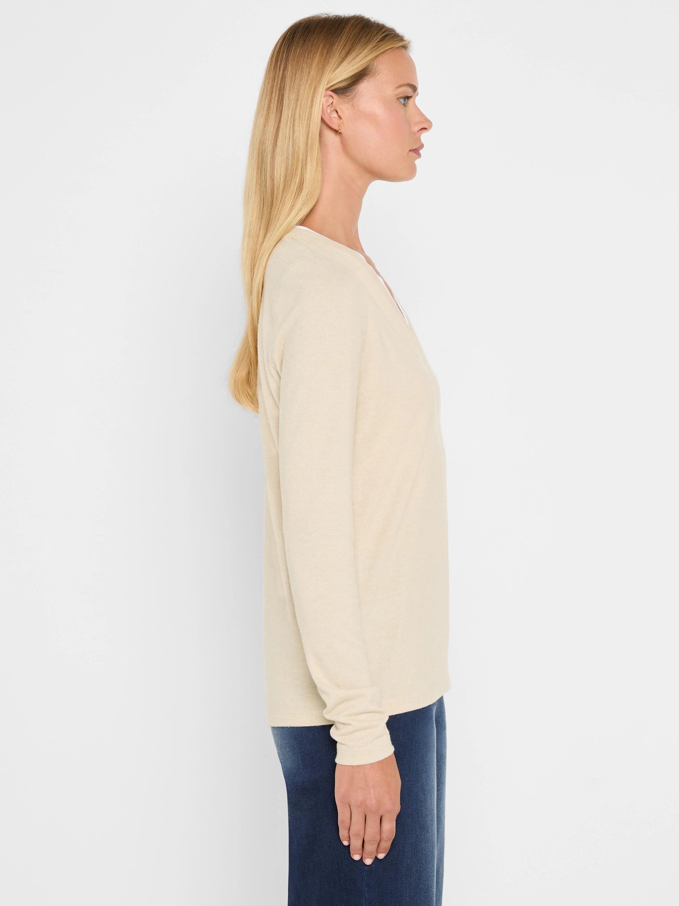 Light beige long-sleeve jersey tee with a double-layer split V-neck. Model shown in profile.