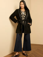 Black wool top coat, mid-length, with a shawl collar, tied waist belt, and dark contrast trim.