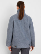 Back view of a muted blue-grey wool coat with a high stand collar and two dark buttons on the wide hem.