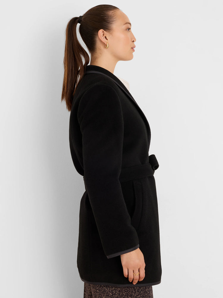 Black belted wool top coat with smooth texture. Dark trim reveals a subtly patterned reverse side at the lapel, cuffs,...