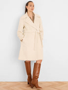 Cream wrap coat with wide lapels, tie belt, soft texture, and functional pockets. Reaches above the knee.