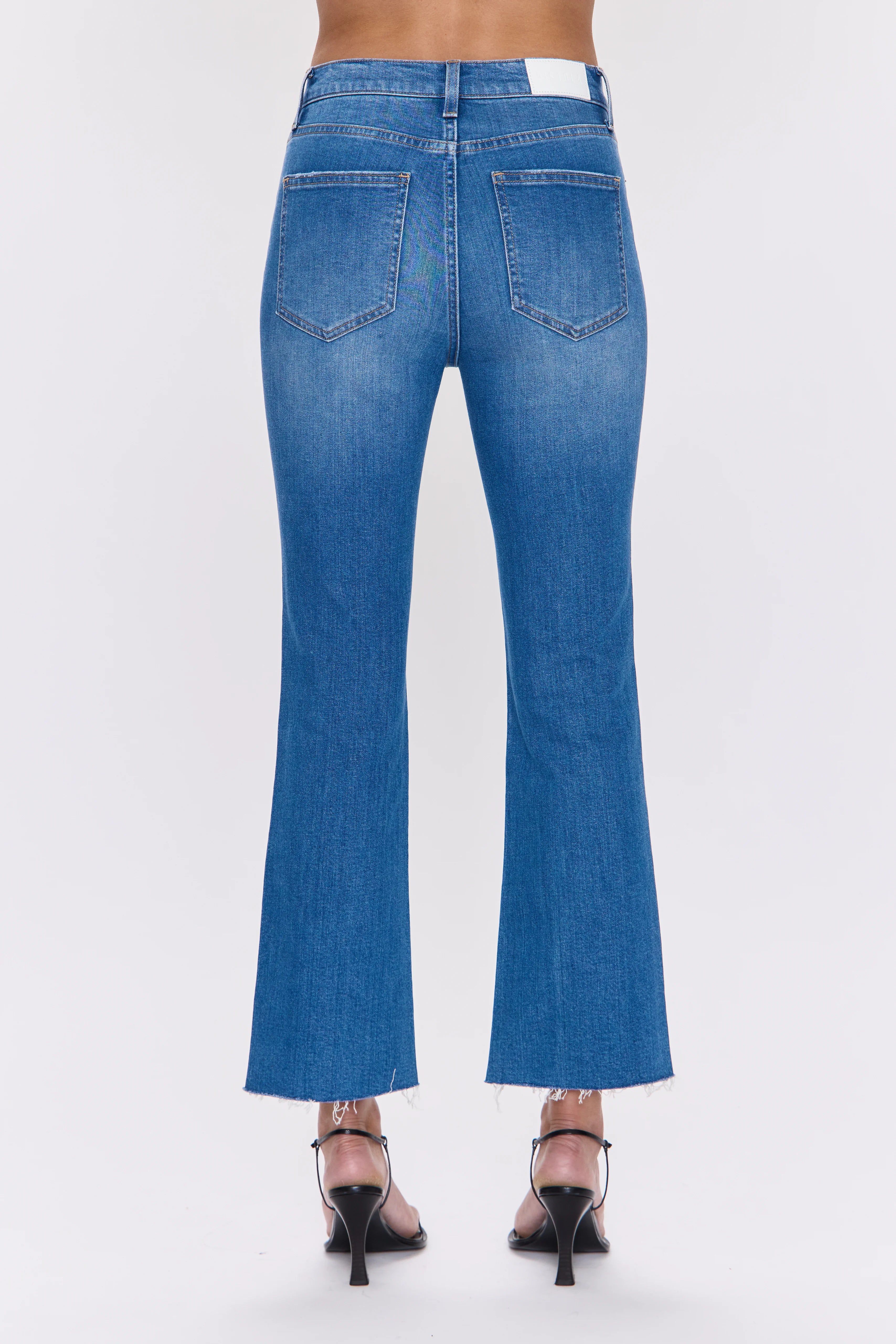 Medium blue denim high-rise crop boot jeans, back view, with subtle fading, back pockets, and raw frayed hems.