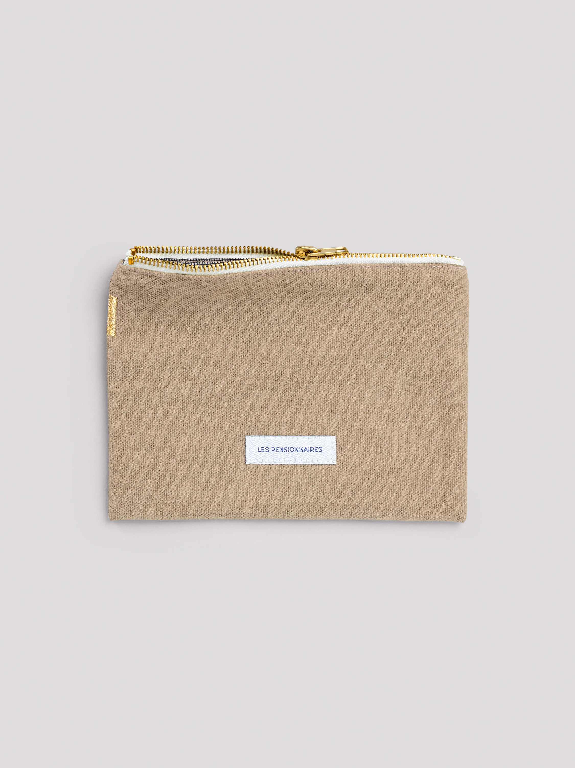 Beige cotton zipper pouch with a gold metal zipper, white "LES PENSIONNAIRES" label, and a gold embroidered stripe.