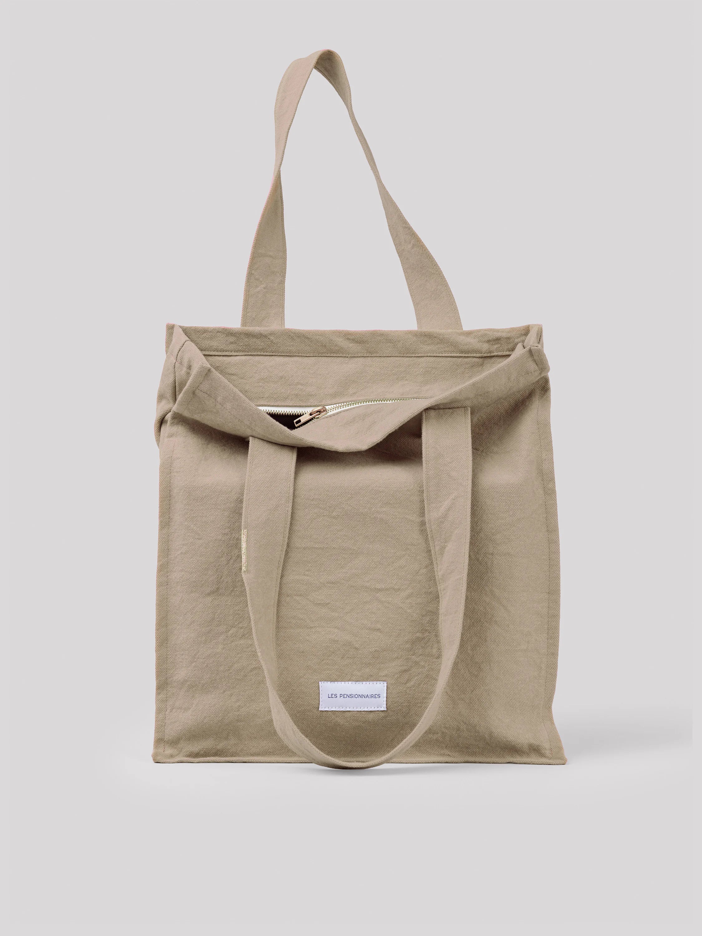 Beige cotton tote bag with two top handles and a partially open zipper closure.
