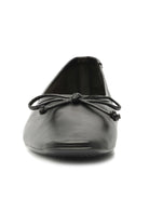 Black leather slip-on flats have a slightly square toe and a matching knotted bow detail.