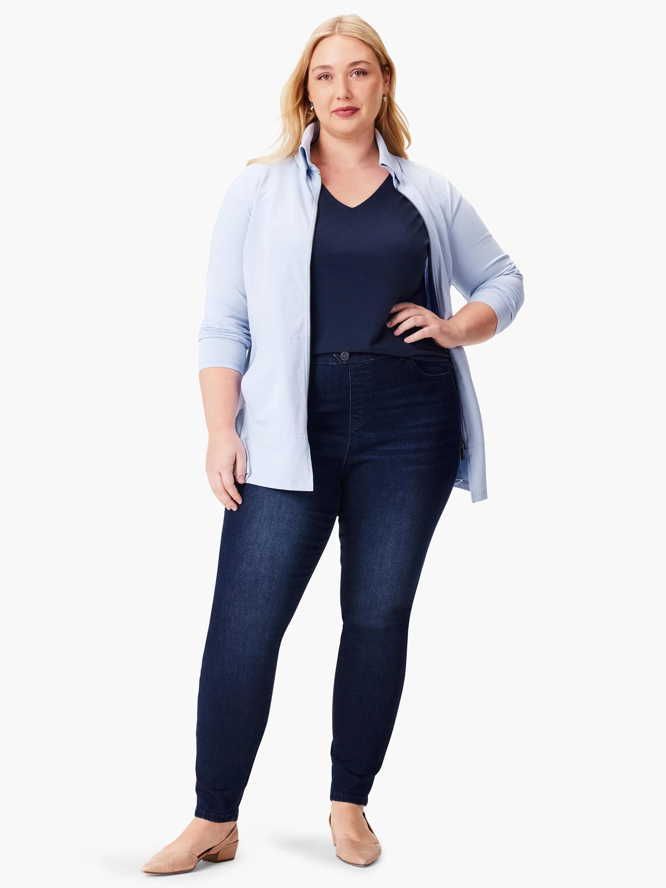 Woman in light blue zip-up jacket over dark navy top and dark wash jeans.  Neutral-toned shoes.