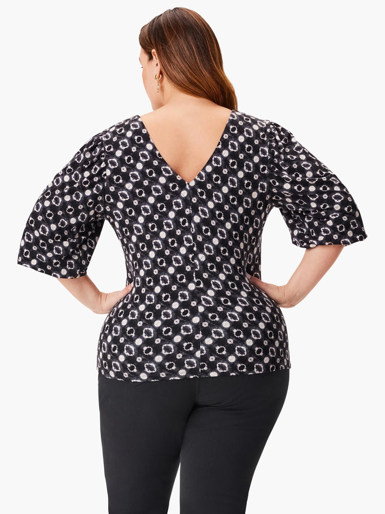 Black top with a V-neck and 3/4 sleeves.  Features a repeating pattern of off-white and dark gray circles on a black...