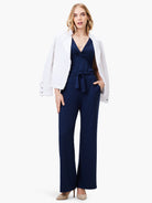Navy blue wide-leg jumpsuit with twisted neckline; belted waist.  Model wears off-white jacket.