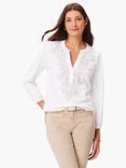 White long-sleeve top with a light gray embroidered floral design down the front.  Henley-style placket.