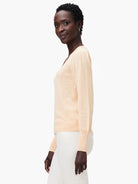 Peach-colored slub knit V-neck sweater with long sleeves.