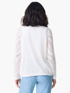 Off-white pointelle sweater;  long sleeves with pointelle detailing on the upper arms.  The back is shown.