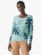 Light blue sweater with dark blue and gold leaf pattern on a textured background. Long sleeves, round neck.