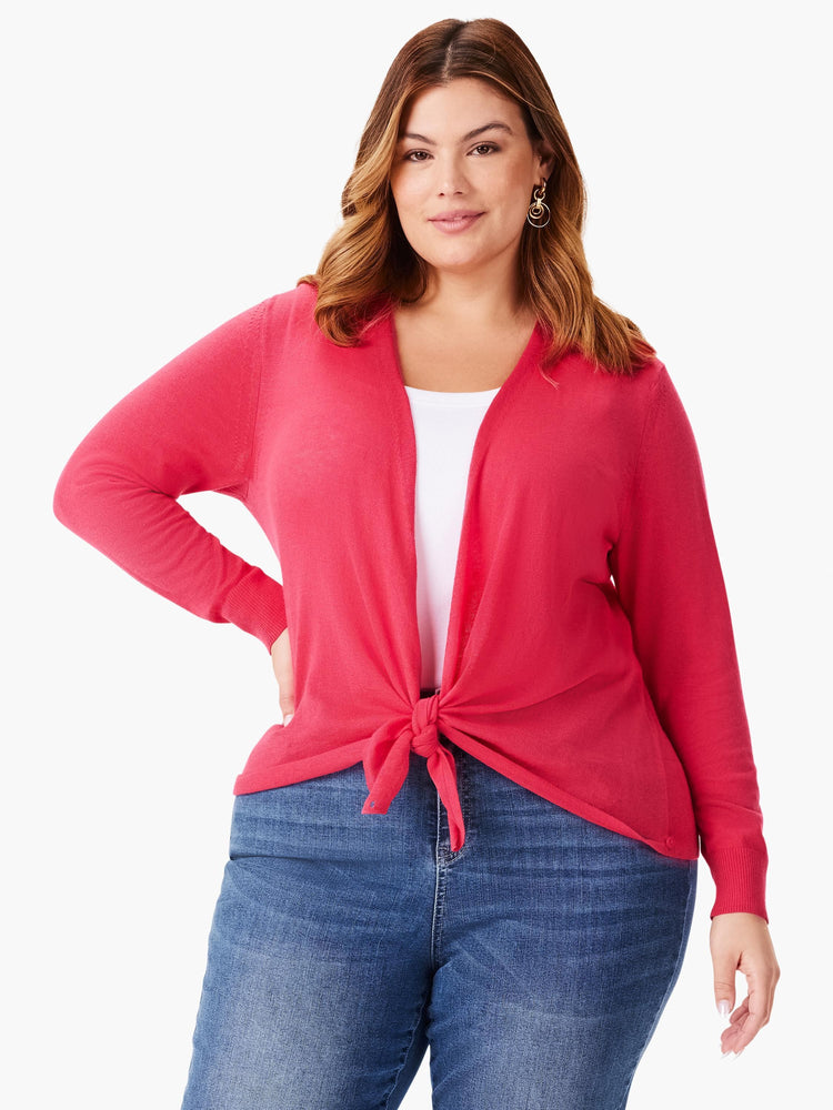 Coral pink open cardigan with long sleeves, knotted at the waist over a white top and blue jeans.