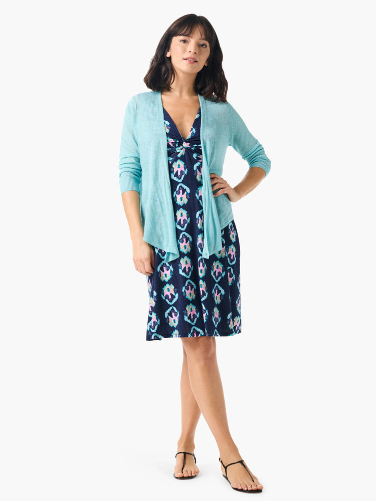 Woman in teal cardigan over navy dress with teal, pink, and white batik print. Knee-length A-line silhouette.