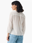 Off-white blouse with pleated back, eyelet detailing at shoulders and neckline. Three-quarter sleeves.