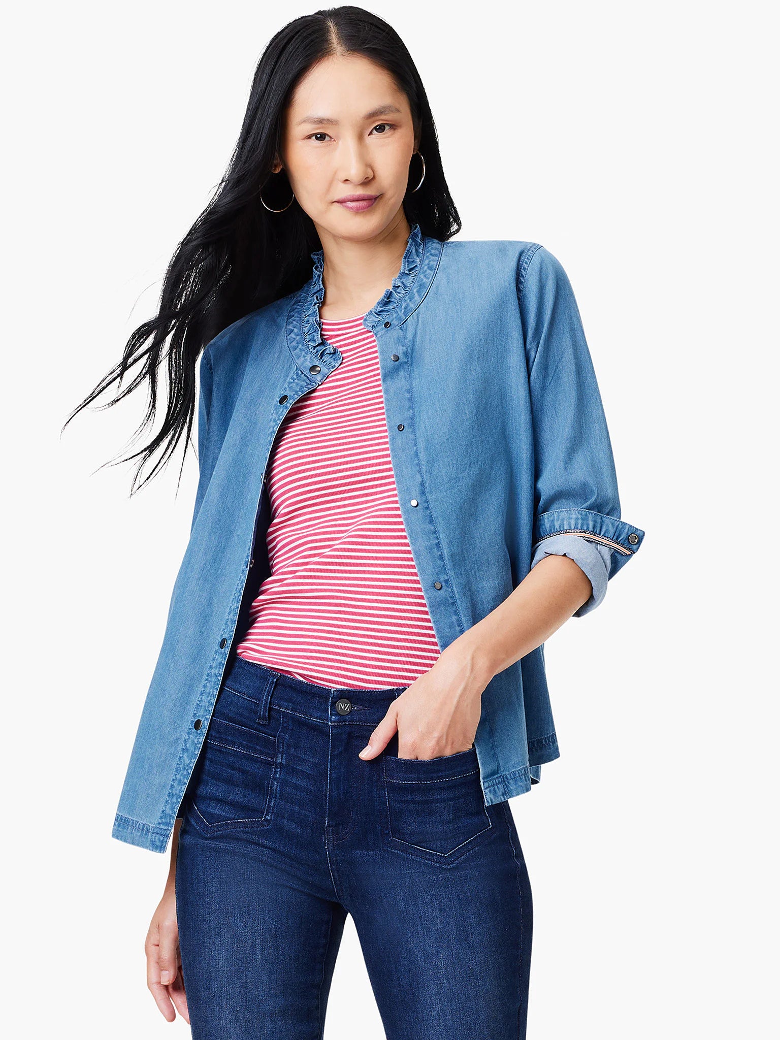 Light blue denim shirt with ruffle neck detail. Model also wears pink and white striped shirt and dark wash jeans.