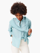 Light blue relaxed-fit button-down shirt with long sleeves, visible white buttons, and a slightly crinkled texture.