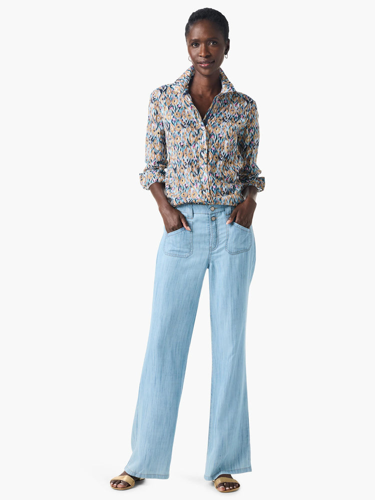 Woman wearing long-sleeve button-down shirt with blue, tan, pink, and black abstract print.  Light blue wide-leg pants...