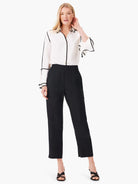 Off-white shirt with black trim, long sleeves, and ruffled cuffs.  Model also wears black pants and shoes.