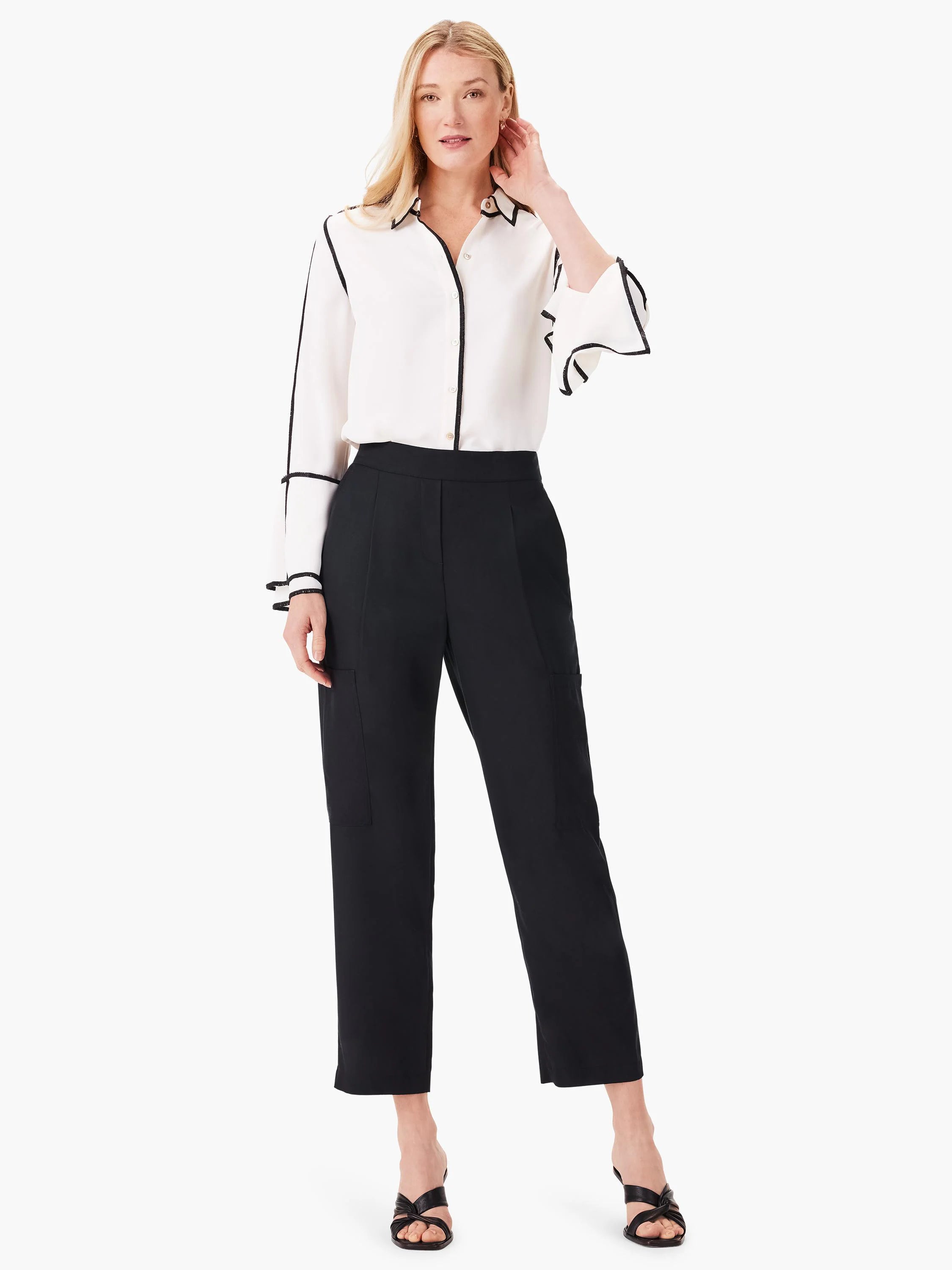 Off-white shirt with black trim, long sleeves, and ruffled cuffs.  Model also wears black pants and shoes.