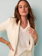 Model wears a relaxed cream blazer with notched lapels over a textured ivory V-neck sweater.