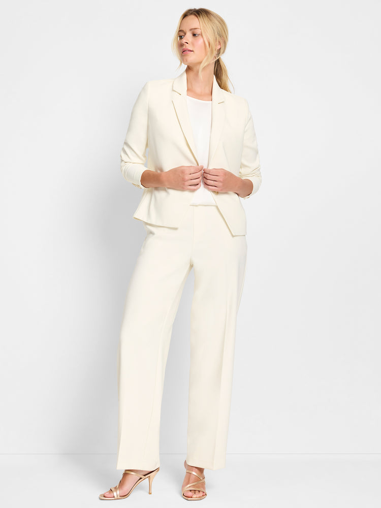 Model wears an off-white tailored suit featuring a fitted blazer and high-waisted wide-leg trousers.