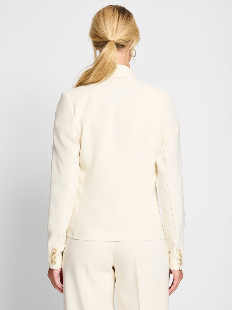 Back view of a model wearing a tailored cream blazer featuring three marbled cuff buttons.