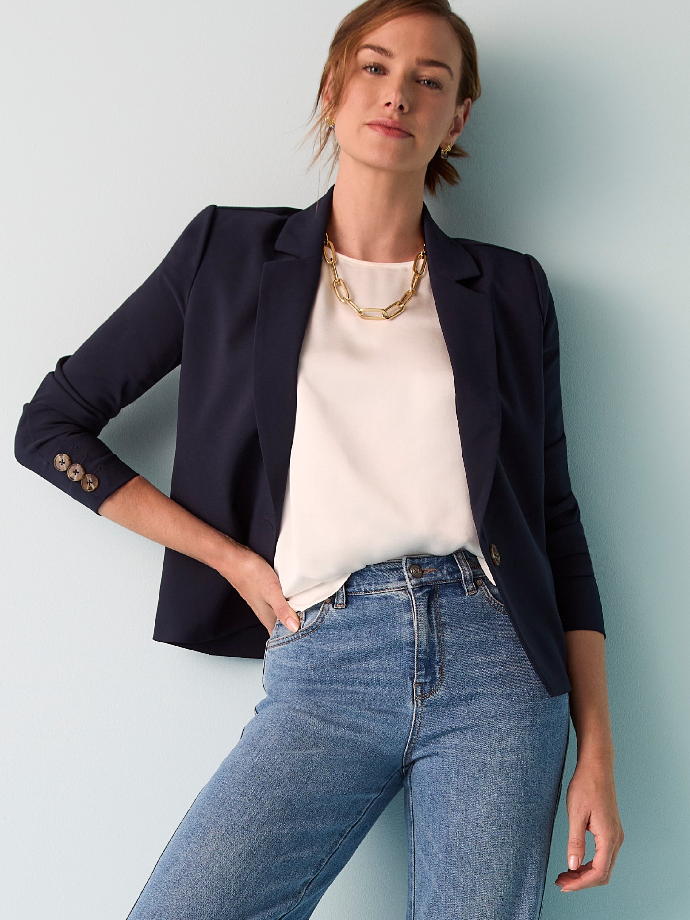 A dark navy fitted blazer features rolled three-quarter sleeves accented by decorative cuff buttons.