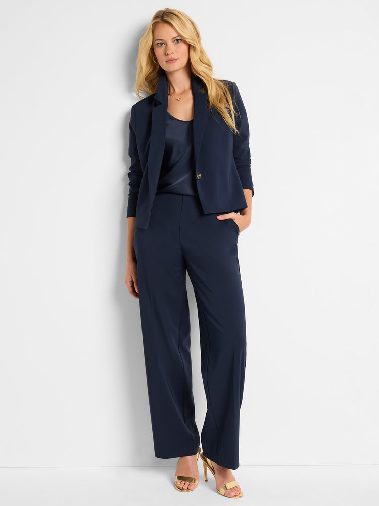 A model wears a navy blue tailored suit featuring a cropped, single-button blazer and flowing wide-leg trousers.