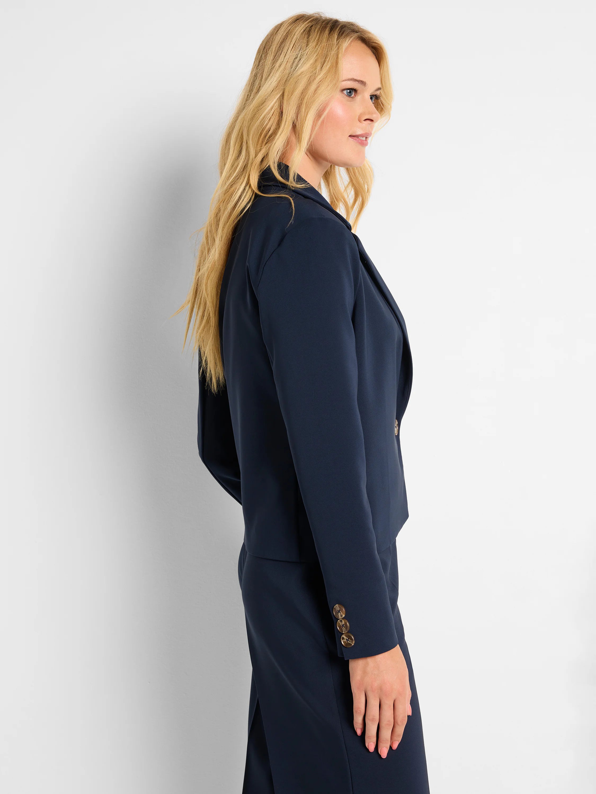 Dark navy blazer with lapels, worn open. Three brown buttons adorn each sleeve cuff.
