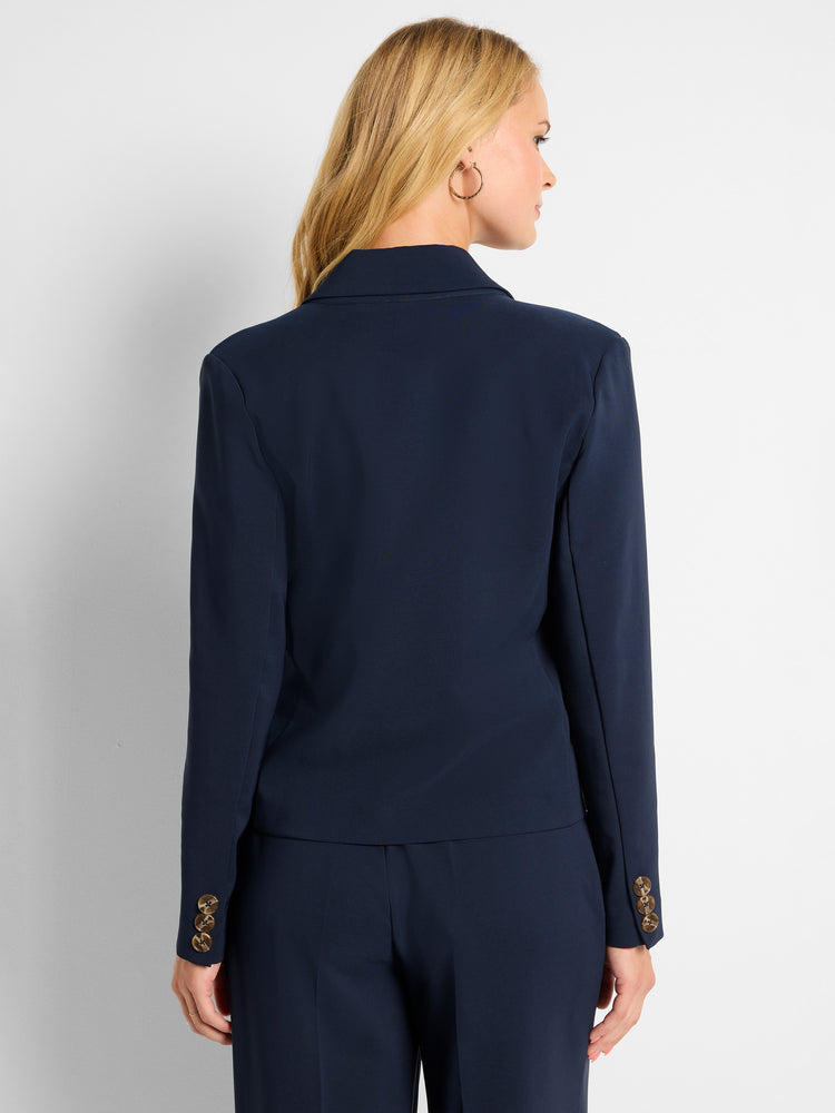 A fitted navy blazer is shown from the back, featuring a structured fit and three decorative tortoiseshell buttons on the.