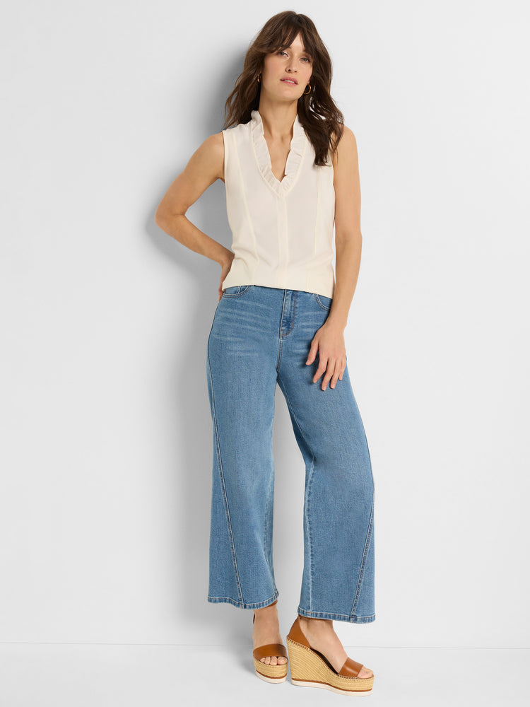 Ivory sleeveless blouse with ruffled V-neckline worn with high-waisted wide-leg blue jeans.